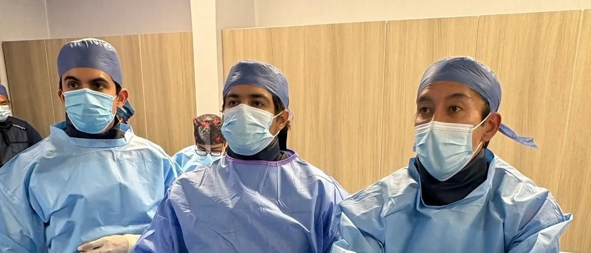 Tres cardiólogos del equipo con bata estéril durante un procedimiento en sala de hemodinamia